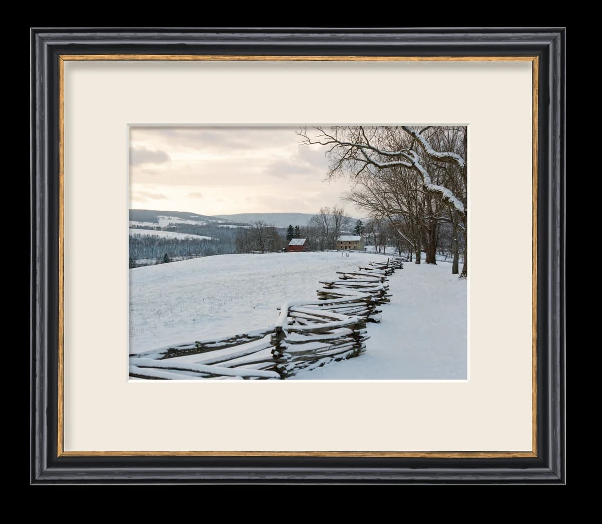 A winter farm landscape print in a black frame with a gold inner lip and a cream mat