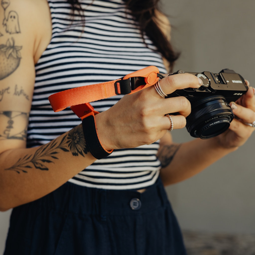 Person holding a camera with an ibis color cuff, wearing a striped shirt Person holding a camera with an ibis color cuff, wearing a striped shirt