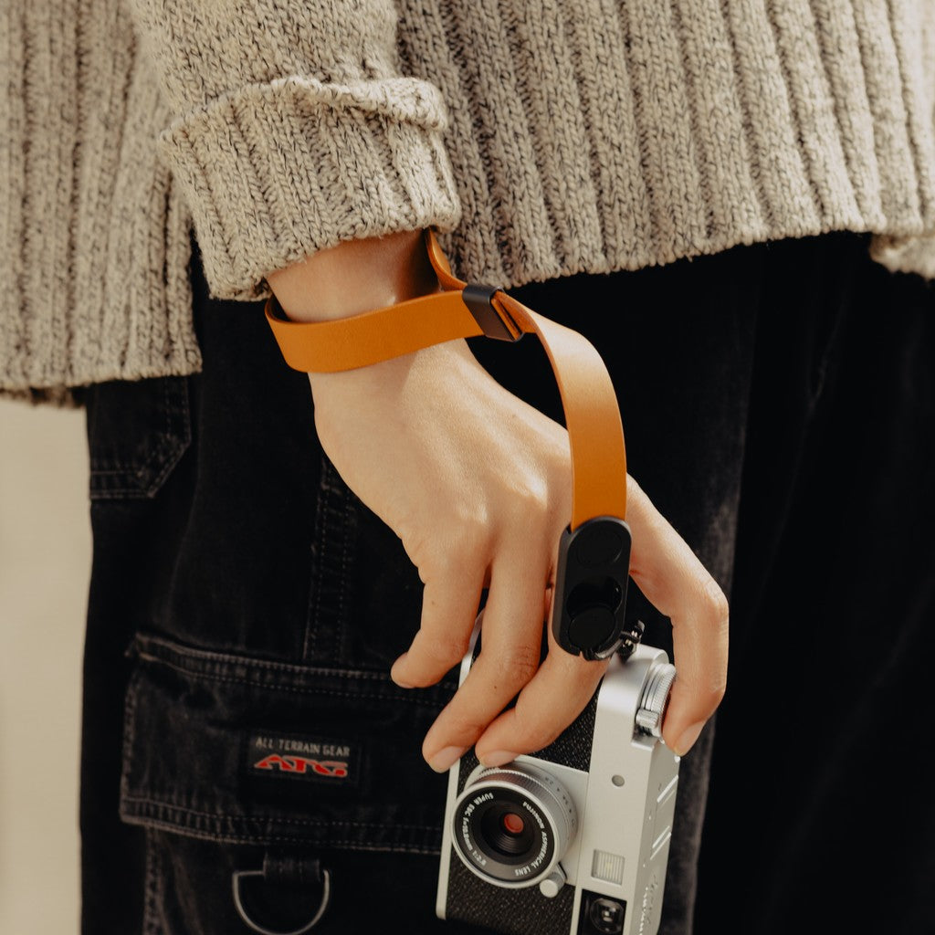 Person wearing a beige sweater holding a camera attached to Amber Leather Cuff Person wearing a beige sweater holding a camera attached to Amber Leather Cuff