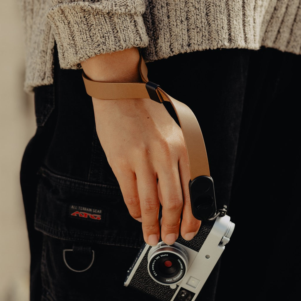 Person holding a camera with a Tan Leather Cuff, wearing a textured sweater and dark pants. Person holding a camera with a Tan Leather Cuff, wearing a textured sweater and dark pants.